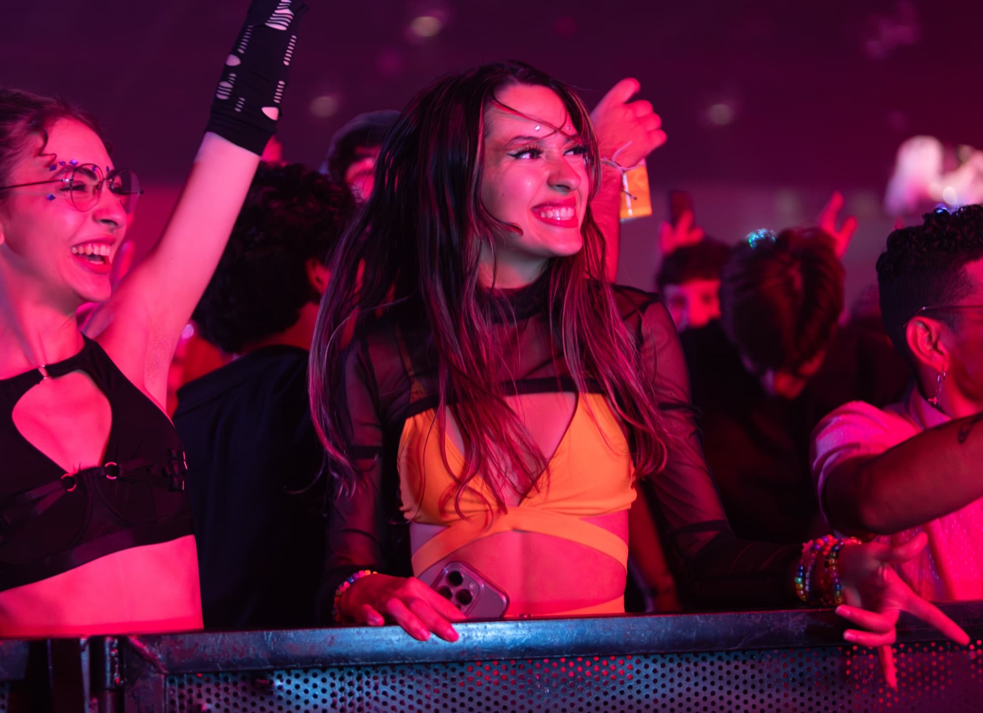 Raver in an orange wrap top smiling under pink light