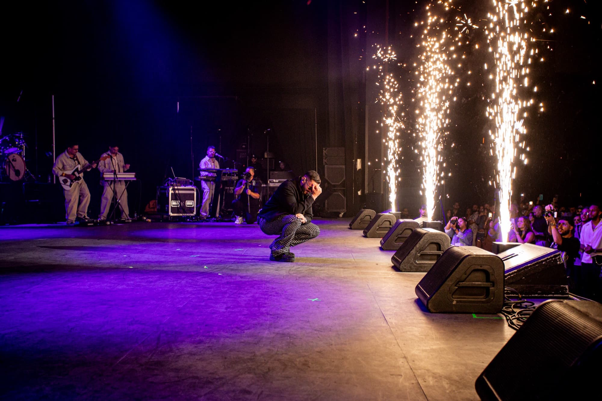 Artist crouched at the stage edge beside a fountain of sparks