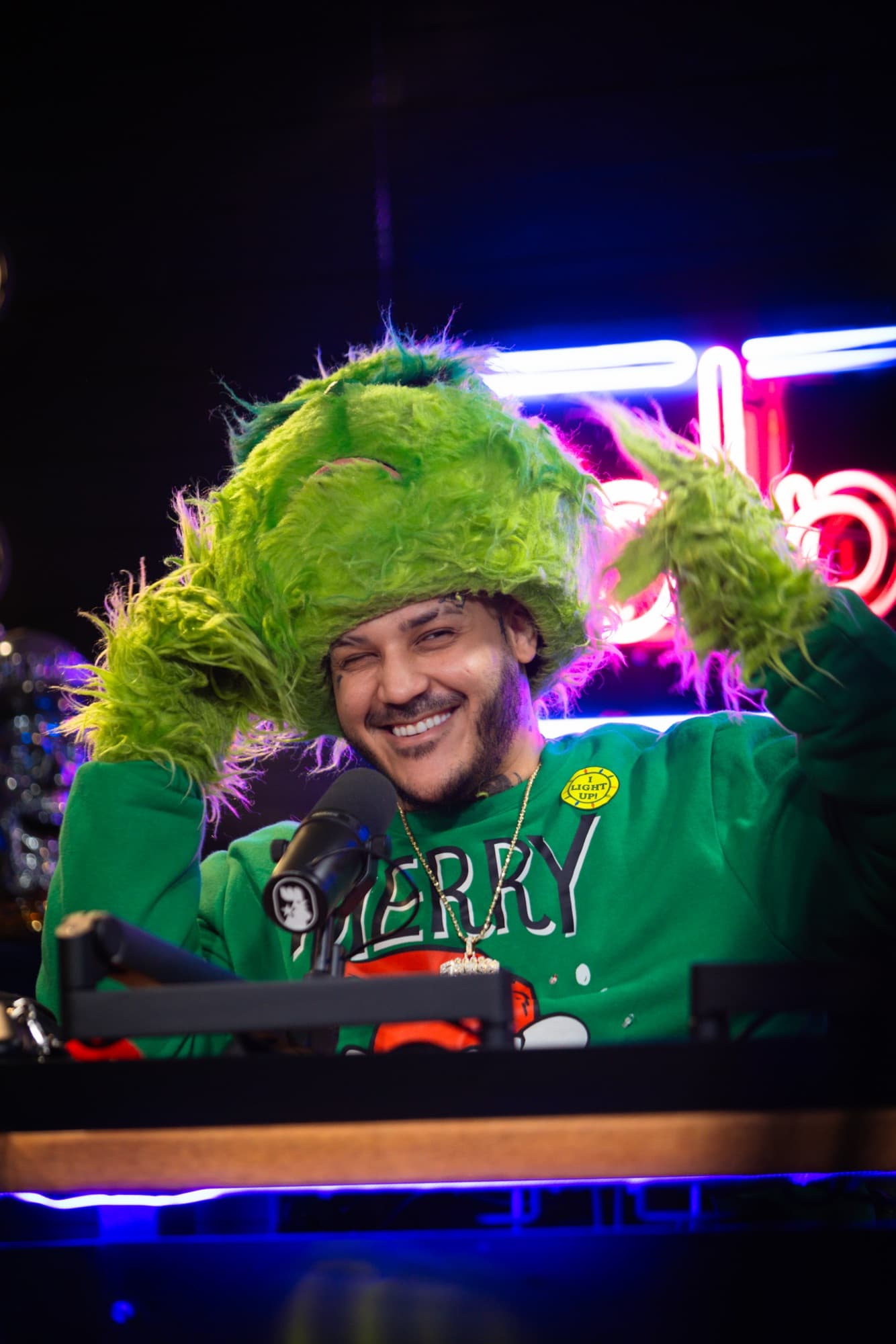 Host laughing in a green Grinch costume on a neon set