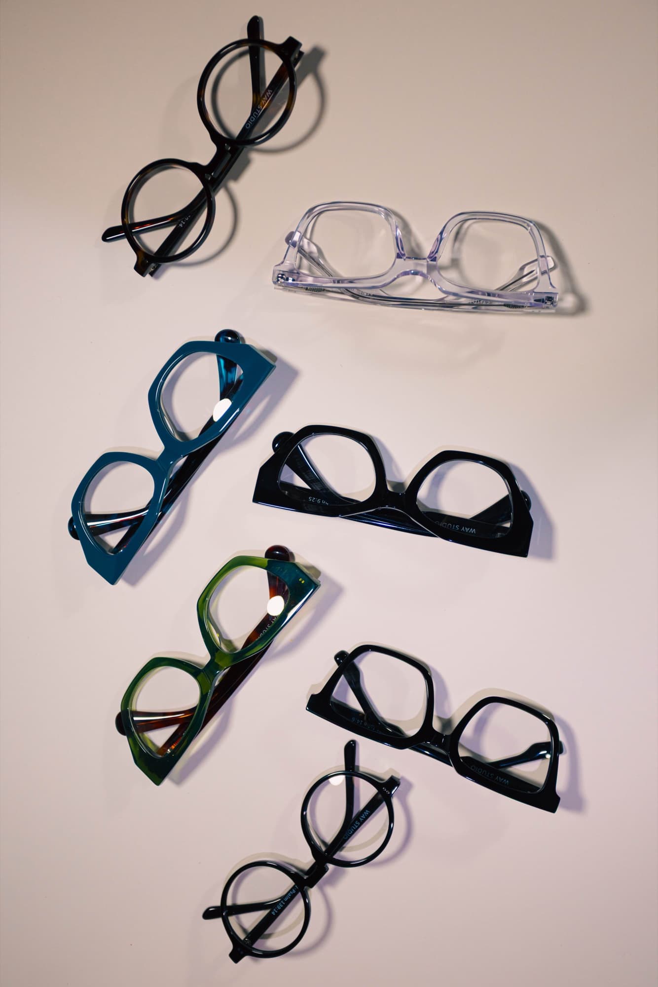 Seven eyeglass frames arranged on a warm neutral surface