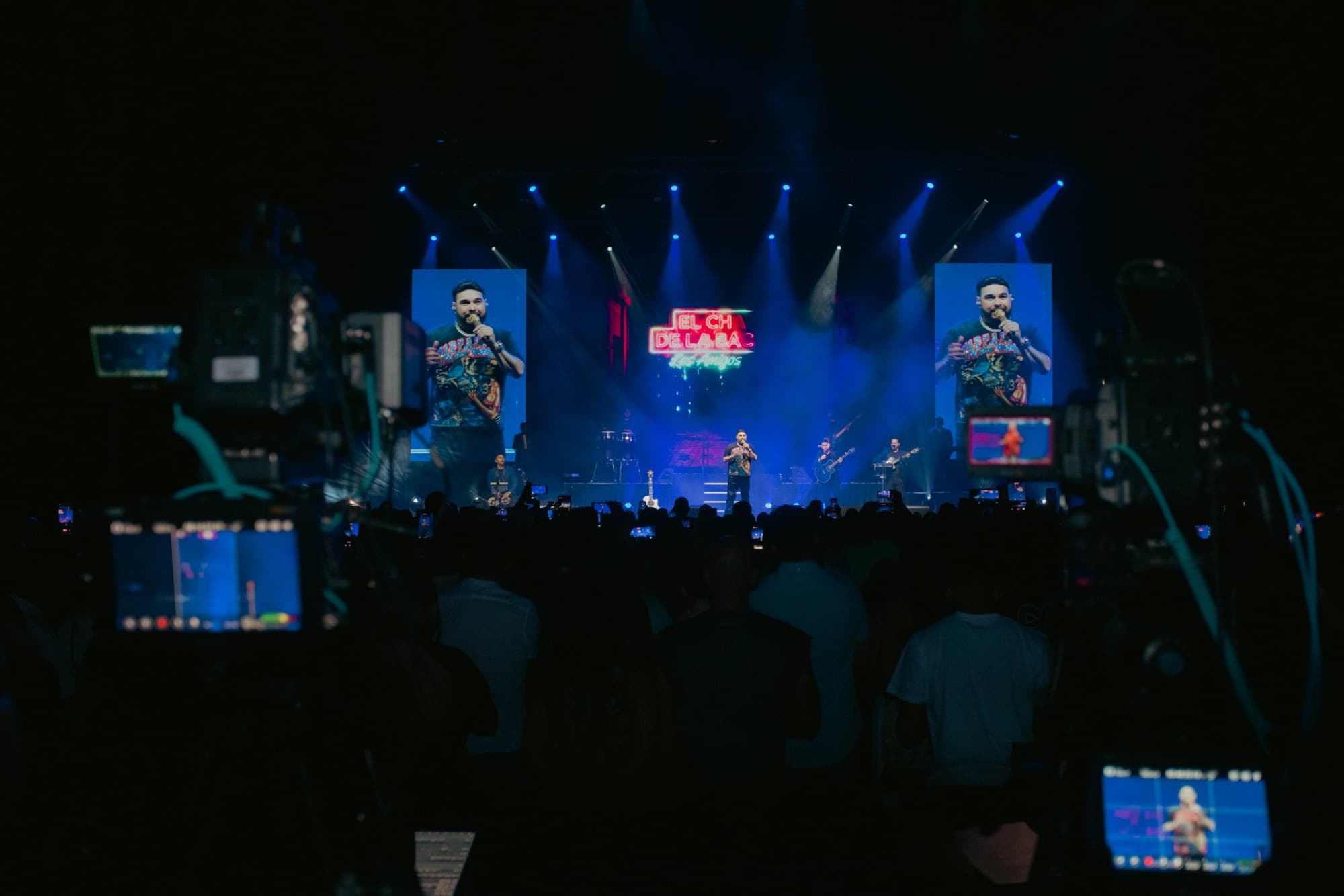 Blue-lit stage flanked by screens, shot over the crowd