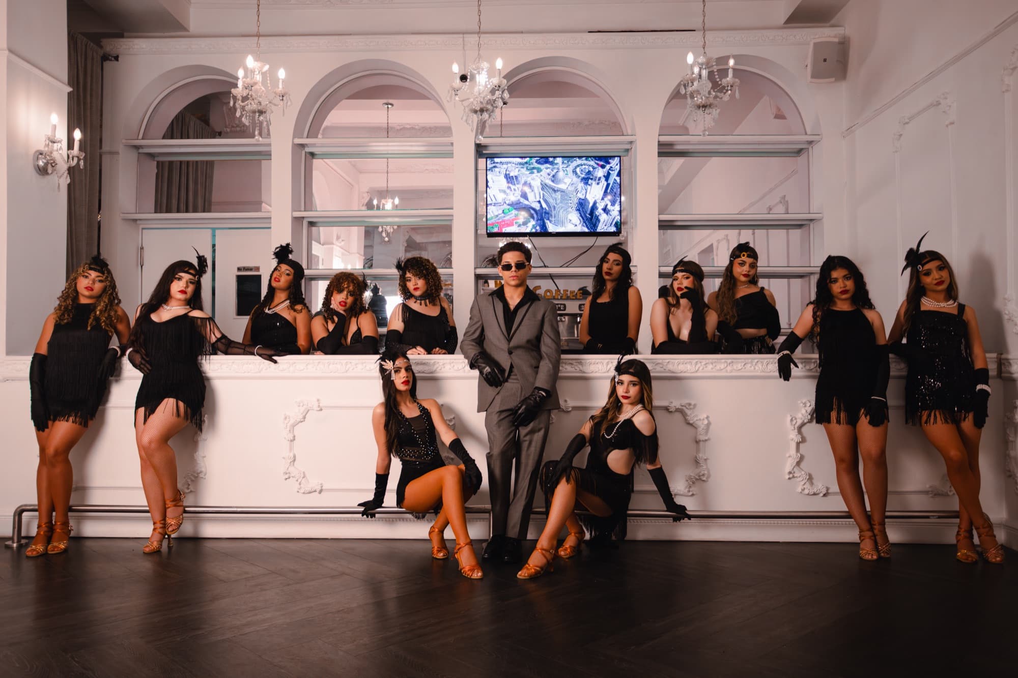 Dance company in black posed across a white ballroom
