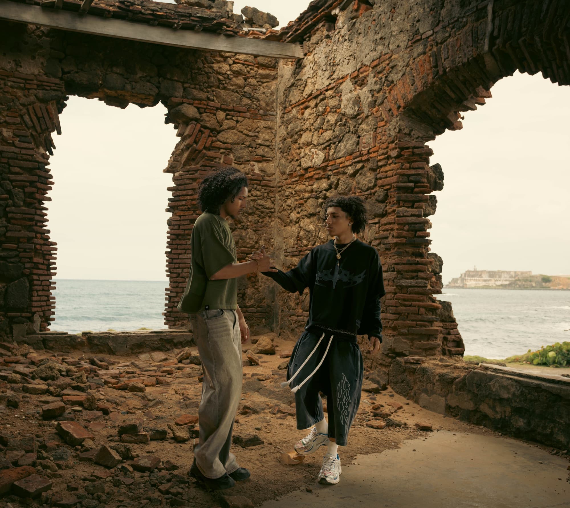 Two models joining hands inside seaside brick ruins