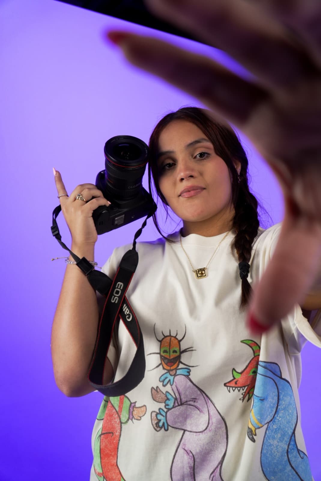 Salomé reaching toward the lens with her camera in hand, purple backdrop