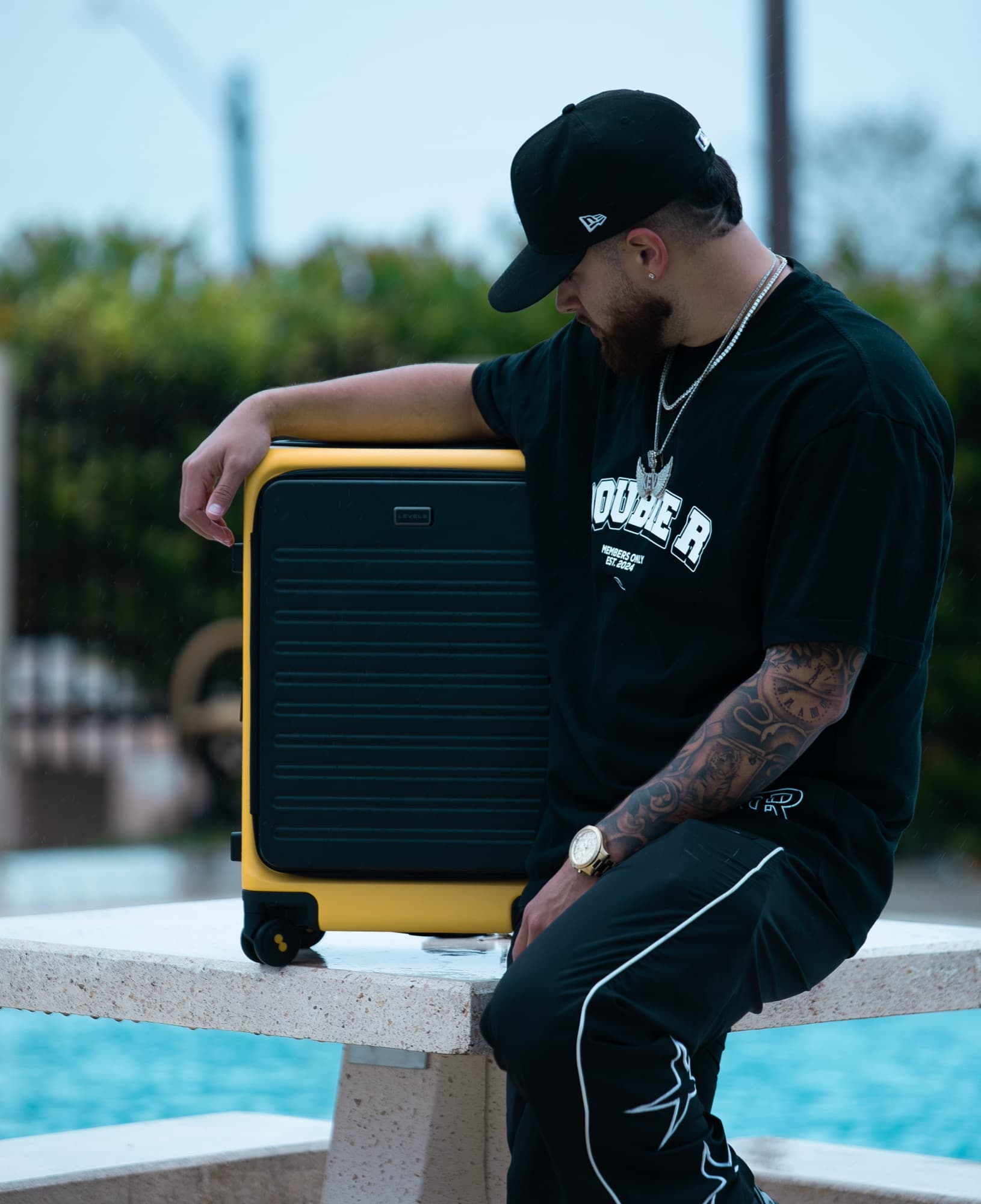 Man resting his arm on a yellow suitcase beside a pool