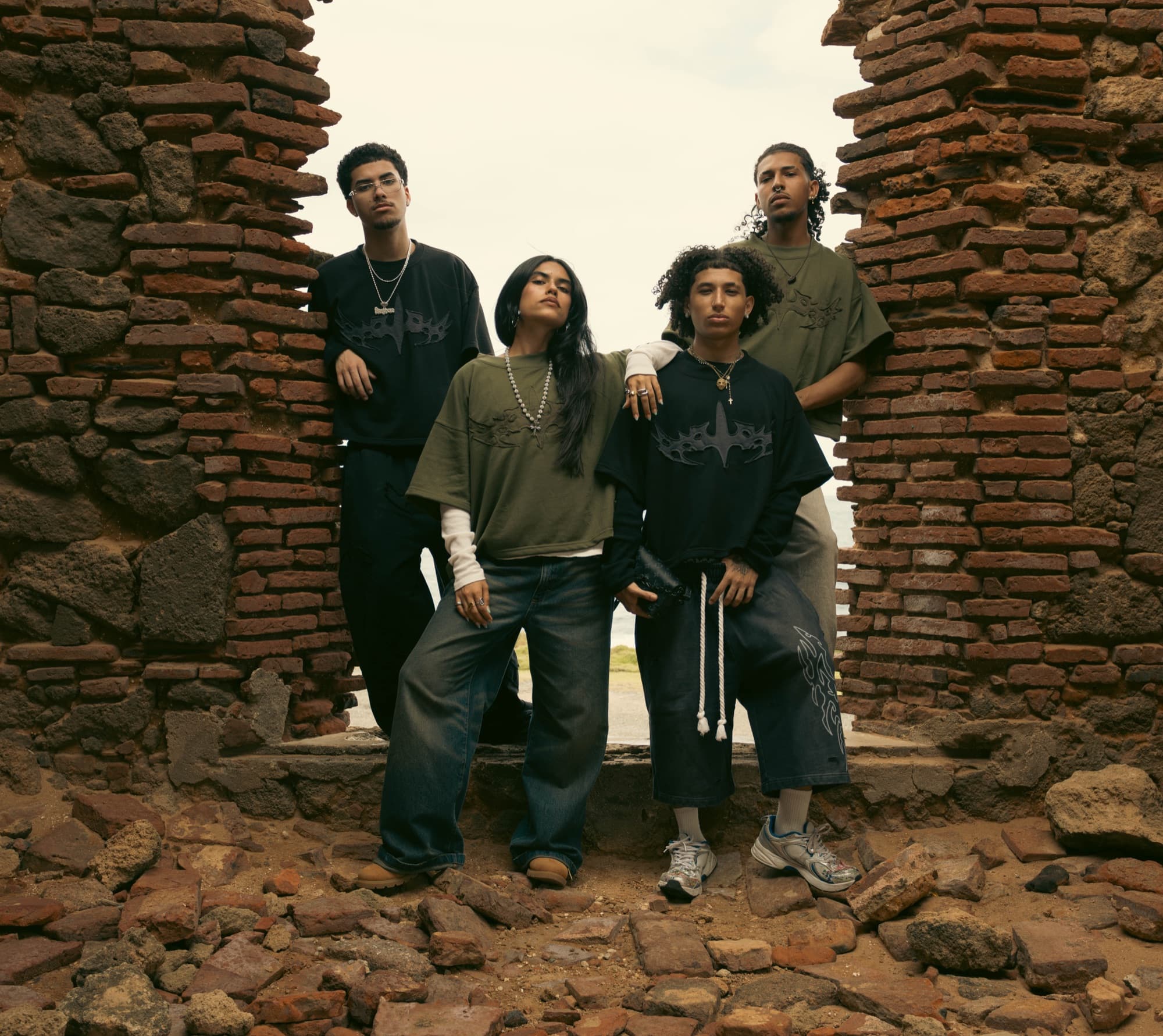 Four models in baggy streetwear framed by a brick ruin doorway
